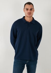 Camisa polo de manga larga en color marino con cuello, cierre de dos botones y una textura suave. Combinada con unos jeans de mezclilla oscuros.