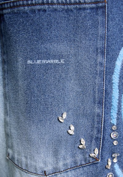 Jeansstoff mit einer hellblauen Waschung, verziert mit dekorativen Strasssteinen und Stickereien. Verwaschene Akzente im Bereich der Tasche.