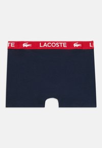 Boxer shorts blu navy con un elastico rosso in vita, caratterizzati dal marchio e dal logo "LACOSTE" in bianco. Materiale in cotone morbido, design di lunghezza intermedia.