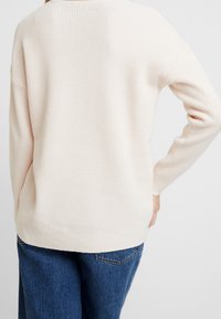 Lichtroze, gestructureerde gebreide trui met lange mouwen en geribde zoom. Licht oversized pasvorm, gedetailleerd met een wafelgebreid patroon aan de achterkant.