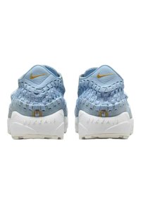 Nike sneakers met een lichtblauwe geweven bovenkant, witte tussenzool en gouden accenten, die een gestructureerd ontwerp met onderscheidende patronen tonen.