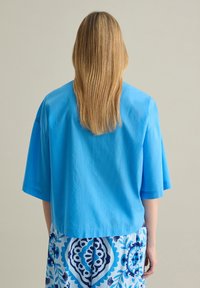 Top corto de color azul claro con mangas anchas y cortas, hecho de un tejido suave. Combinado con pantalones de estampado azul y blanco que presentan diseños florales.