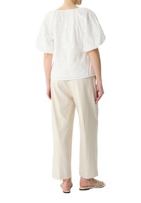 Weiße bestickte Bluse mit Puffärmeln, kombiniert mit beigen maßgeschneiderten Hosen und Riemchensandalen. Der Stoff hat ein strukturiertes Blumenmuster.