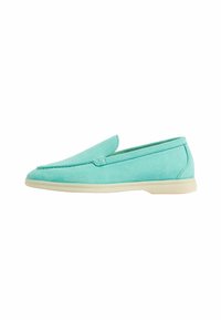 Zapato slip-on de gamuza aqua con una textura suave, punta redondeada y una suela de goma color crema en contraste. Diseño simple y elegante sin acentos adicionales.