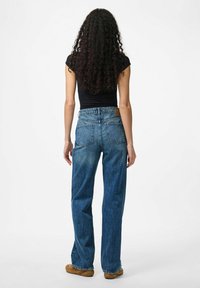 Traperice visokog struka u plavoj boji s ravnim nogavicama, s istanjenim pranjem, dva stražnja džepa i kožnom označavalo na pojasu.