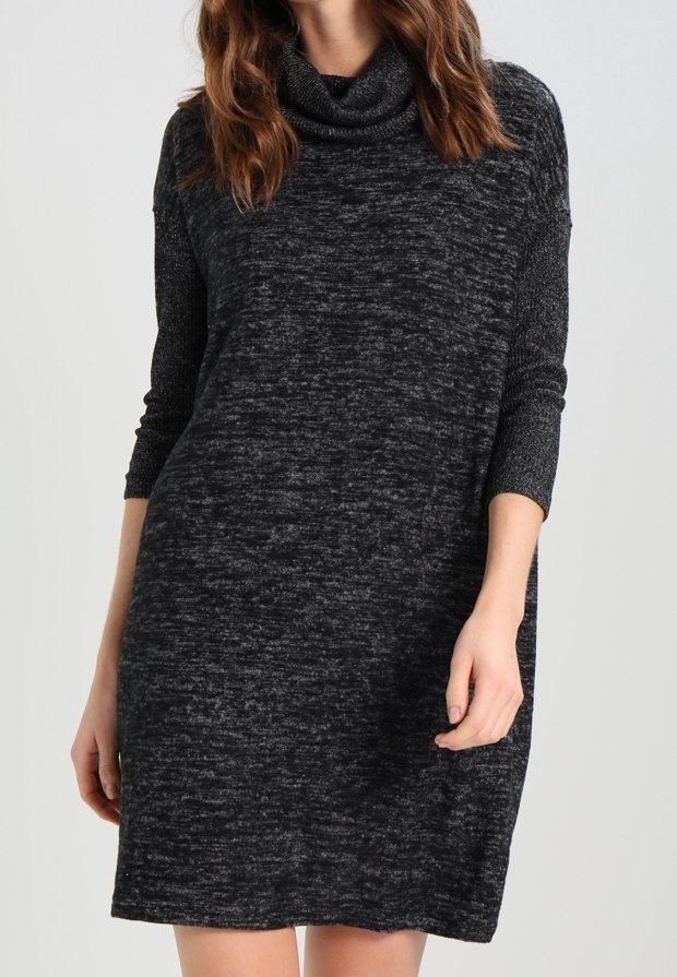Femme portant une robe en maille gris foncé, à manches longues, arrivant au genou, avec un col roulé ample.