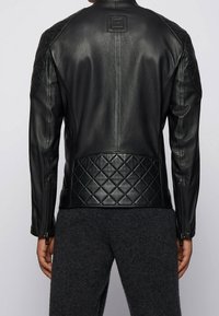 Černá kožená bunda se stehovanými panely na ramenech a spodní části zad, s hladkou texturou, zapínáním na zip a logovou visačkou.