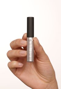 Rossetto liquido argento in un tubo trasparente con cappuccio nero, tenuto in una mano. Il tubo ha una texture glitterata con una finitura liscia.