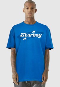 Zila kokvilnas T-kreklu ar īsām piedurknēm, ar "Starboy" logo baltā fontā, ar grafiskajiem elementiem un zvaigznēm apļa dizainā.