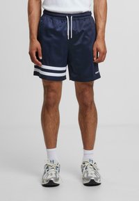 Shorts de sport bleu marine en tissu léger, avec des rayures blanches sur les côtés, une taille élastique et un cordon de serrage.