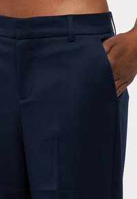 As calças ajustadas azul marinho apresentam uma textura suave, um bolso lateral e uma cintura limpa. O tecido parece leve e formal.