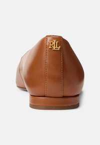 Barna bőrből készült lapos cipő, lekerekített orral és visszafogott sarokkal. Arany „RL” logó a hátsó részen, varrott varrással díszítve.