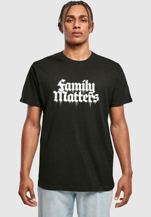 T-shirt en coton noir avec du texte blanc indiquant "La famille, c'est important" dans une police audacieuse et stylisée. Manches courtes et design décontracté.