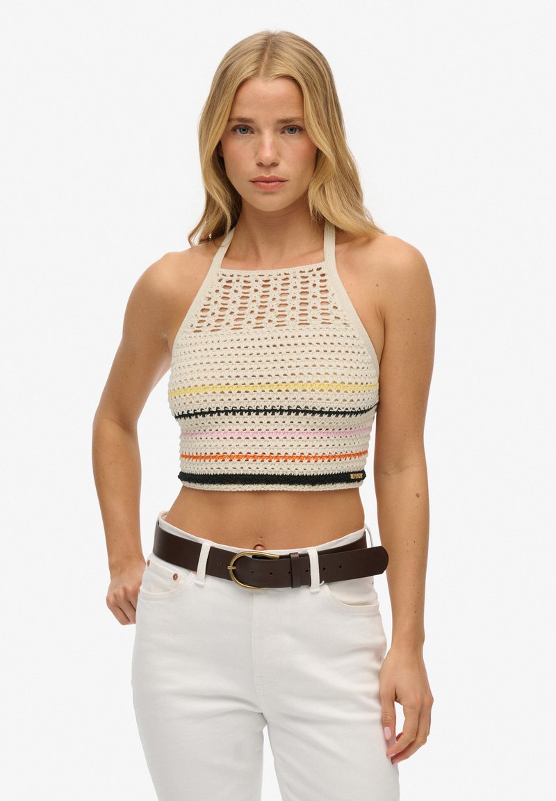 Gehaakt haltertop met variërende gekleurde strepen (oranje, roze, geel) en een open brei-design; gecombineerd met hoge witte jeans en een bruine riem.