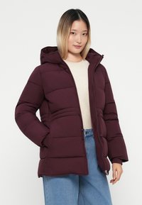 Burgundy puffer jacket with a hood, featuring a zip closure and front pockets, made from quilted material for insulation and comfort.