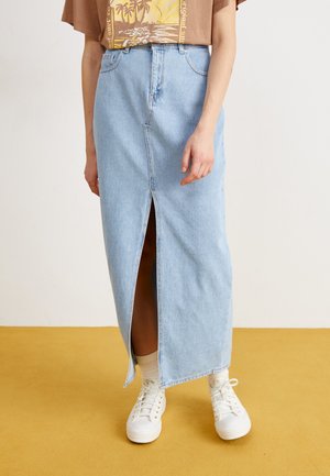Lichtblauwe denim maxi-rok met een split aan de voorkant, hoge taille en riemlussen, gecombineerd met witte sneakers en enkelkousen.