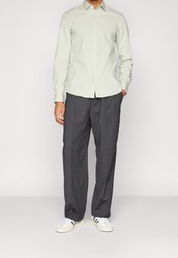 Lichtgroen overhemd met lange mouwen, met knopen, gecombineerd met donkergrijze broek met streepjes en witte sneakers met grijze strepen.