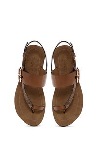 Sandalias de cuero marrón con suela plana. Cuentan con una tira ancha que cruza el pie y una tira texturizada en el dedo del pie. Cierre con hebilla ajustable.