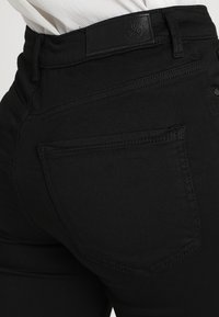 Jean noir taille haute avec une texture lisse, des poches latérales et arrière, et des détails de couture subtils sur les coutures.