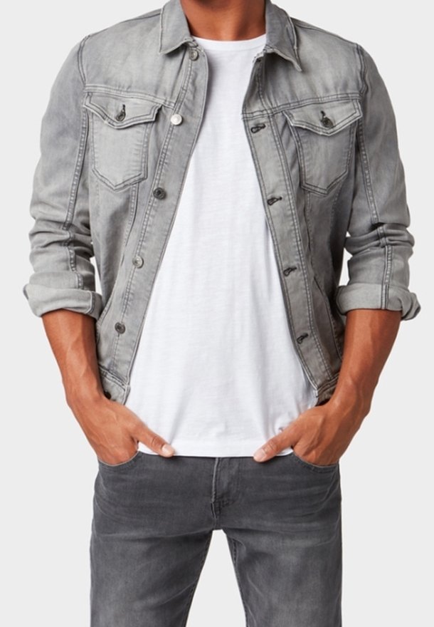 Grå denimjacka med knapplås, fickor med klaff och uppvikta ärmar, bärs över en vit t-shirt och tillsammans med grå jeans.