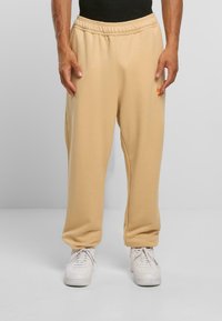 Bēša Nike sporta bikses ar elastīgu jostasvietu un sānu kabatām, kas rotātas ar oranžu logo uz kreisā gurnu. Gluda, kokvilnas maisījuma audums.