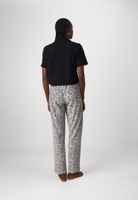 Zwarte top met korte mouwen en een textuurpatroon, gecombineerd met lichtgekleurde broek met een bloemenprint in rood, groen en zwart.