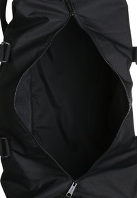 Bolsa de lona negra con apertura con cremallera, textura de tela suave, interior espacioso y correas ajustables para mayor comodidad al transportar.