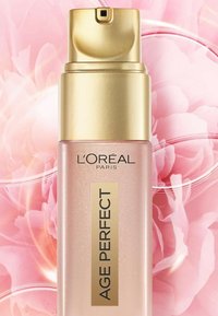 Sérum L'Oréal Age Perfect dans un flacon rose clair avec un bouchon-pompe doré. Présente une étiquette dorée avec un texte noir en gras. Surface texturée avec éclat.