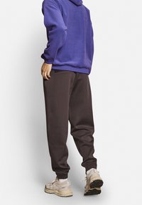 Violetti huppari rentolla istuvuudella, yhdistetty tummanruskeisiin collegehousuihin. Housuissa on joustavat resorit ja taskut, ja ne on yhdistetty neutraaleihin lenkkareihin.