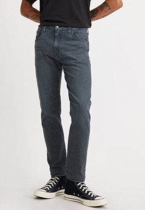 Donkergrijze jeans van denimstof, met een slim fit, vijfzakkenontwerp en subtiele vervaging, gecombineerd met zwarte hoge sneakers.