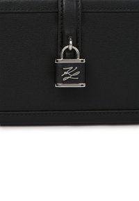 Czarna skórzana torebka o eleganckim designie, z polerowanym, srebrnym zamkiem z detalem logo oraz precyzyjnym przeszyciem wzdłuż krawędzi.