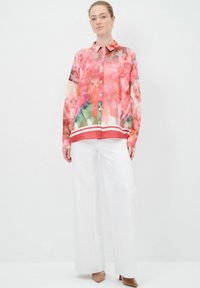 Camicia button-up colorata con motivo astratto, dotata di colletto e taschino sul petto; abbinata a pantaloni bianchi a gamba larga e tacchi color beige.