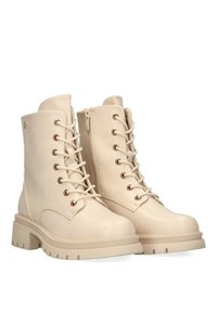 Botas de tobillo beige hechas de material sintético suave. Cuenta con ojales de metal, cordones en la parte delantera y una suela gruesa y texturizada.