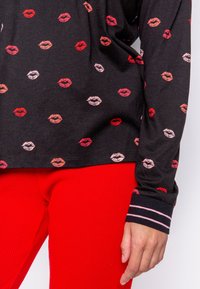 Svart långärmad topp med flerfärgad läpptrycksdesign; har en ribbad manschett med rosa och vita ränder. Kombineras med röda ribbade byxor.