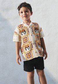 Virkat skjorta med färgglada, kvadratiska mönster inklusive djurmotiv. Kortärmad, knappar framtill, kombinerad med svarta shorts.