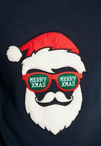 Marineblauw sweater met een pluizig witte Santa-gezicht, rode hoed en groene zonnebril met de tekst "MERRY XMAS". Geweven stof en felle kleuren.