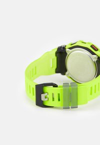 Montre avec un bracelet en silicone vert, dotée d'une boucle noire, d'un dos métallique et d'une surface texturée avec des fentes de ventilation.