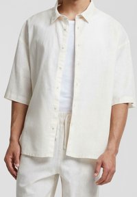 Camicia a maniche corte, aperta sul davanti, in lino color crema chiaro con vestibilità rilassata. Presenta una chiusura con bottoni e una texture liscia. Abbina pantaloni coordinati.