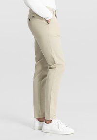 Beżowe bawełniane spodnie chino o slim fit z bocznymi kieszeniami i zapinaną na guzik tylną kieszenią. W połączeniu z białymi sneakersami, prezentujące czysty design.