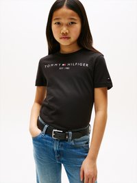 Μαύρο βαμβακερό t-shirt με το κείμενο "TOMMY HILFIGER ΕΣΤ. 1985" εκτυπωμένο στα λευκά. Συνδυασμένο με μπλε τζιν παντελόνι και μαύρη ζώνη με ασημένια αγκράφα.
