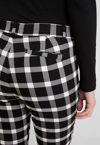 Pantalons à carreaux noirs et blancs avec une coupe ajustée, dotés de poches arrière et d'une ceinture. Le tissu a une texture lisse.
