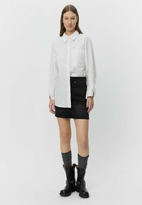 White long-sleeve shirt with large collar, single chest pocket; black denim miniskirt with textured pattern; knee-high black boots with silver accents.