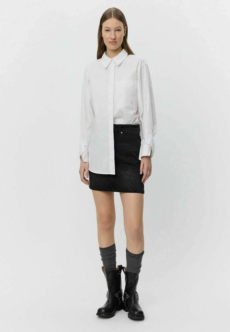 White long-sleeve shirt with large collar, single chest pocket; black denim miniskirt with textured pattern; knee-high black boots with silver accents.