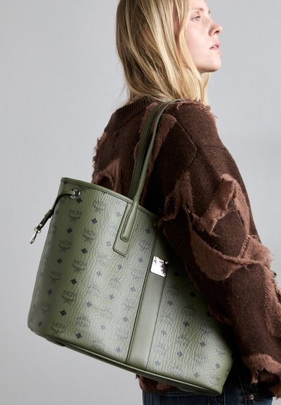 Green leather tote bag with embossed logo pattern, silver hardware, and two top handles. Features a textured finish and structured shape.