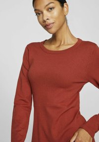Robe longue en tricot rouge à manches longues, avec un col rond et une silhouette ajustée. La texture est lisse avec de subtils détails en côtes.