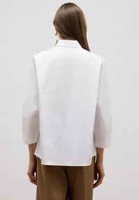 Chemise blanche légère avec un design structuré, dotée de manches trois-quarts, d'un col et d'un ourlet droit.