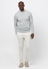 Helles graues Zip-Up-Pullover, cremefarbene Chinos und beigefarbene Schuhe. Weicher Baumwollstoff, figurbetontes Design mit einer glatten Silhouette und minimaler Detailgestaltung.