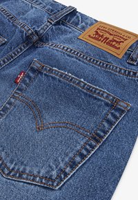 Μπλε τζιν παντελόνι με υφή στην επιφάνεια, διαθέτοντας πορτοκαλί ραφές, πίσω τσέπη με σχέδιο σε σχήμα καρδιάς και δερμάτινο λογότυπο σε καφέ χρώμα.