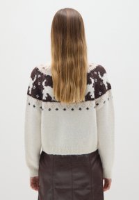Weißer Strickpullover mit einem gemusterten braunen Schulterbereich, der Rentiere zeigt, und einem gerippten Saum, kombiniert mit einem dunkelbraunen Lederrock.