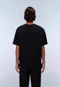 Černé bavlněné tričko, krátké rukávy, kulatý výstřih, volný střih, jednobarevné s hladkouTexturou, zobrazené zezadu.